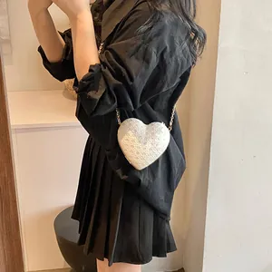Sac bandoulière blanc en forme de cœur avec chaîne dorée porté par un mannequin