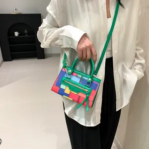 Detail view of colorful geometric patchwork handbag with adjustable green strap and gold zippers