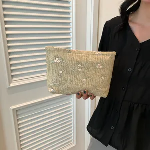 Detailed macro view of woven green clutch bag with white floral embroidery and zipper