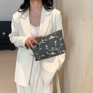 Detail of grey woven clutch bag featuring delicate white floral embroidery and leaf patterns
