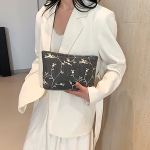 Detail of dark grey woven clutch with white flower embroidery held by a model