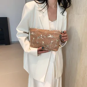 Detailed embroidery of white flowers on a brown woven clutch bag held by a model