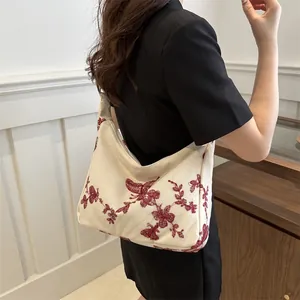 Detail of cream canvas underarm bag with red butterfly embroidery and floral patterns
