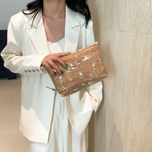 Detail of woven straw clutch bag featuring delicate white flower and leaf embroidery