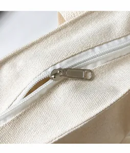 Detail of a smooth silver metal zipper pull on a white canvas tote bag closure