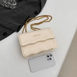 Detailansicht der cremeweißen Tasche mit gewellter Klappe und goldener Kette