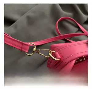Close-up of golden metal lobster clasp and embossed logo on the magenta crossbody bag