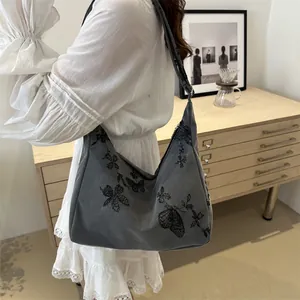 Close-up of a grey hobo bag with black butterfly embroidery and wide shoulder strap