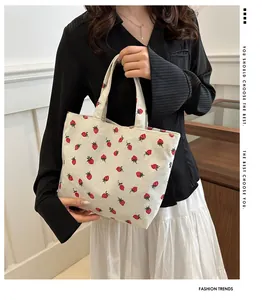 Detail of strawberry corduroy tote bag held by model showing texture and compact size