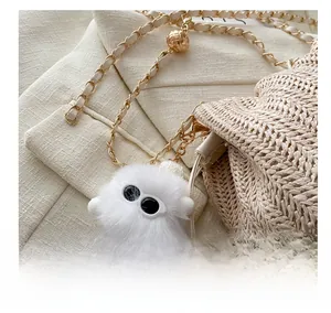 Detail of white plush monster charm with iconic big eyes on straw bucket bag strap