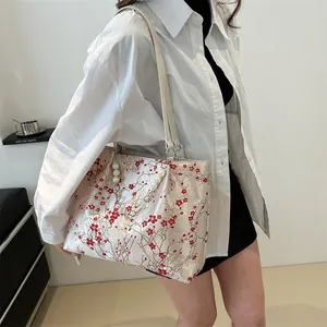 Detail of red plum blossom embroidery and pearl pendant on jacquard shoulder bag