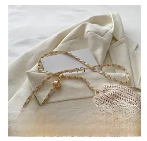 Detail of woven bucket bag featuring a gold chain strap with a textured sphere charm