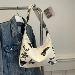 Detail of butterfly and floral embroidery on a cream canvas hobo bag with wide strap
