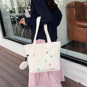 Detail of cream canvas tote bag featuring colorful letter embroidery and mini pouch