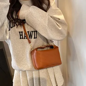 Close-up of caramel PU leather texture and debossed rich rabbit logo on a crossbody bag