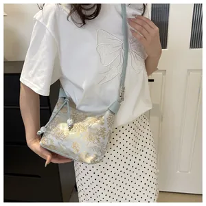 Detail of light blue jacquard crossbody bag with golden floral embroidery and pearl charm