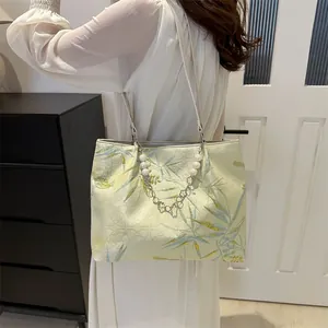 Detail of jacquard tote bag featuring pale yellow leaf patterns and pearl chain strap