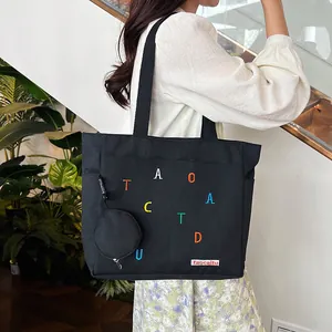 Detail of black canvas tote bag featuring colorful letter embroidery and a mini round coin purse