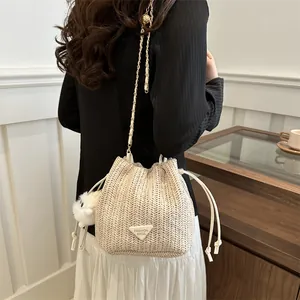 Close-up of beige woven bucket bag featuring人字 texture and plush ball charm accessory