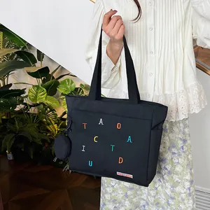 Detail of black canvas tote bag with colorful letter embroidery and small round coin pouch