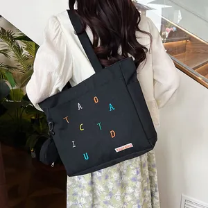 Close-up of black canvas tote bag with colorful letter embroidery and small hanging pouch