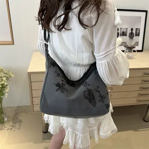 Grey canvas hobo bag with black butterfly embroidery on a woman's shoulder
