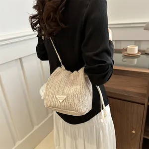 Detailed close-up of straw woven bucket bag with metal chain strap and white pompom charm