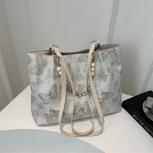 Close-up of butterfly embroidery and pearl charm detail on a large jacquard tote bag
