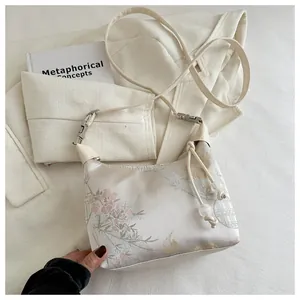 Detailed close-up of bird and floral embroidery on a white satin jacquard shoulder bag