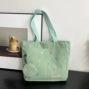 Detailed macro view of light green canvas tote bag featuring floral embroidery and a small pouch