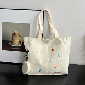Detail of cream canvas tote bag featuring colorful embroidery and a round mini coin purse