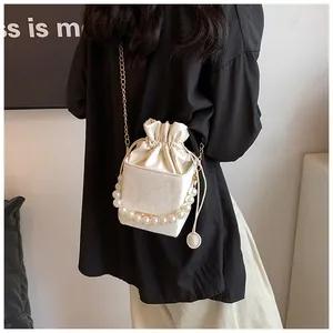 Detail of white drawstring bucket bag with large pearl handle and gold chain strap