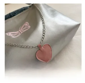 Detail of silver crossbody bag featuring pink butterfly embroidery and heart charm