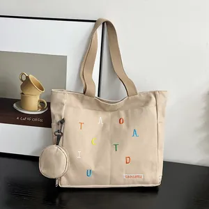 Detail of beige canvas tote bag with letter embroidery and matching mini round pouch
