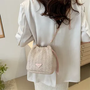 Detail of straw bucket bag featuring pink leather logo plate and chain shoulder strap