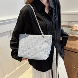Detail of light blue textured tote bag with chain strap worn by a model in a casual setting
