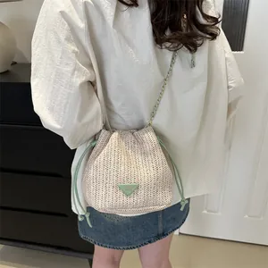 Detailed view of cream straw bucket bag with green triangle logo and chain strap on shoulder