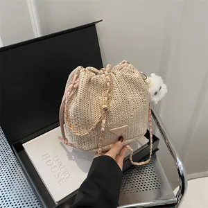 Close-up of woven straw bucket bag with pink leather handle and gold chain strap