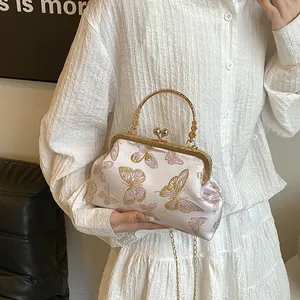 Detail of vintage butterfly embroidery on pink satin handbag with golden floral handle