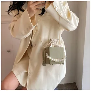 Detail of light green bucket bag featuring a pearl handle and gold chain strap
