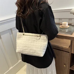 Detail of white tweed shoulder bag with gold chain strap shown on model in a cozy setting