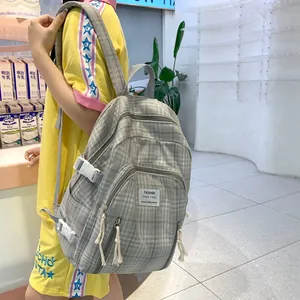 Detailansicht eines grauen Karo-Rucksacks mit Seitenschnallen und weißen Reißverschlüssen