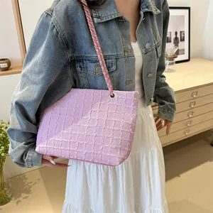 Detail of pink quilted woven shoulder bag with golden chain strap on a wooden cabinet
