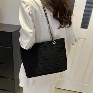 Detail of black tote bag featuring distinctive wave texture and metal chain strap