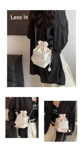 Detail of elegant drawstring bucket bag featuring pearl handle and gold chain strap