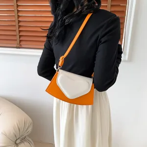 Fashionable heart-shaped crossbody bag with orange base and white flap shown on a model