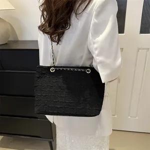 Detail of black tweed shoulder bag with gold chain strap and textured fabric finish
