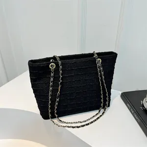 Detail of the black textured tweed fabric and golden chain strap on a women's tote bag