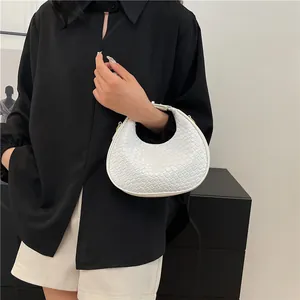 Minimalist white woven crescent handbag styled with a classic black outfit on a model