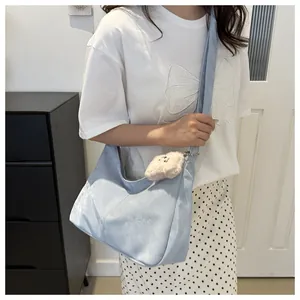 Detail of light blue hobo bag with a cute plush bear pendant shown on model